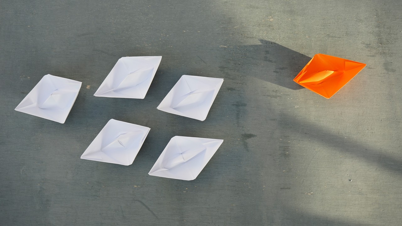 A orange paper boat followed by five white paper boats; image used for investment risk tolerance page.