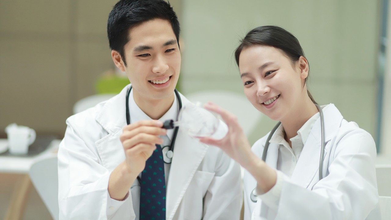 Two doctors are looking at the magnifying glass in a lab; image used for HSBC Taiwan i-invest for online trading page.
