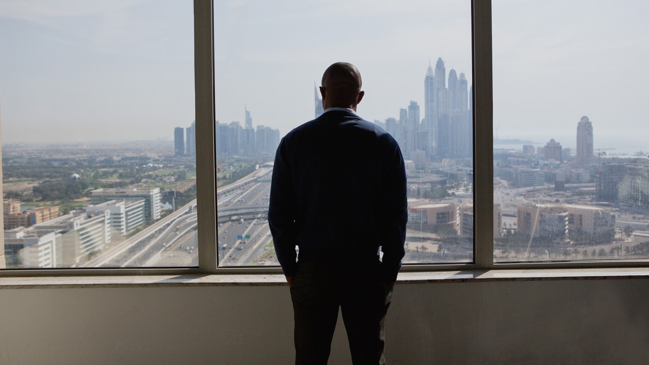 一位男士站在窗前觀看着城市風景；圖片使用於滙豐One能投資講堂頁面。