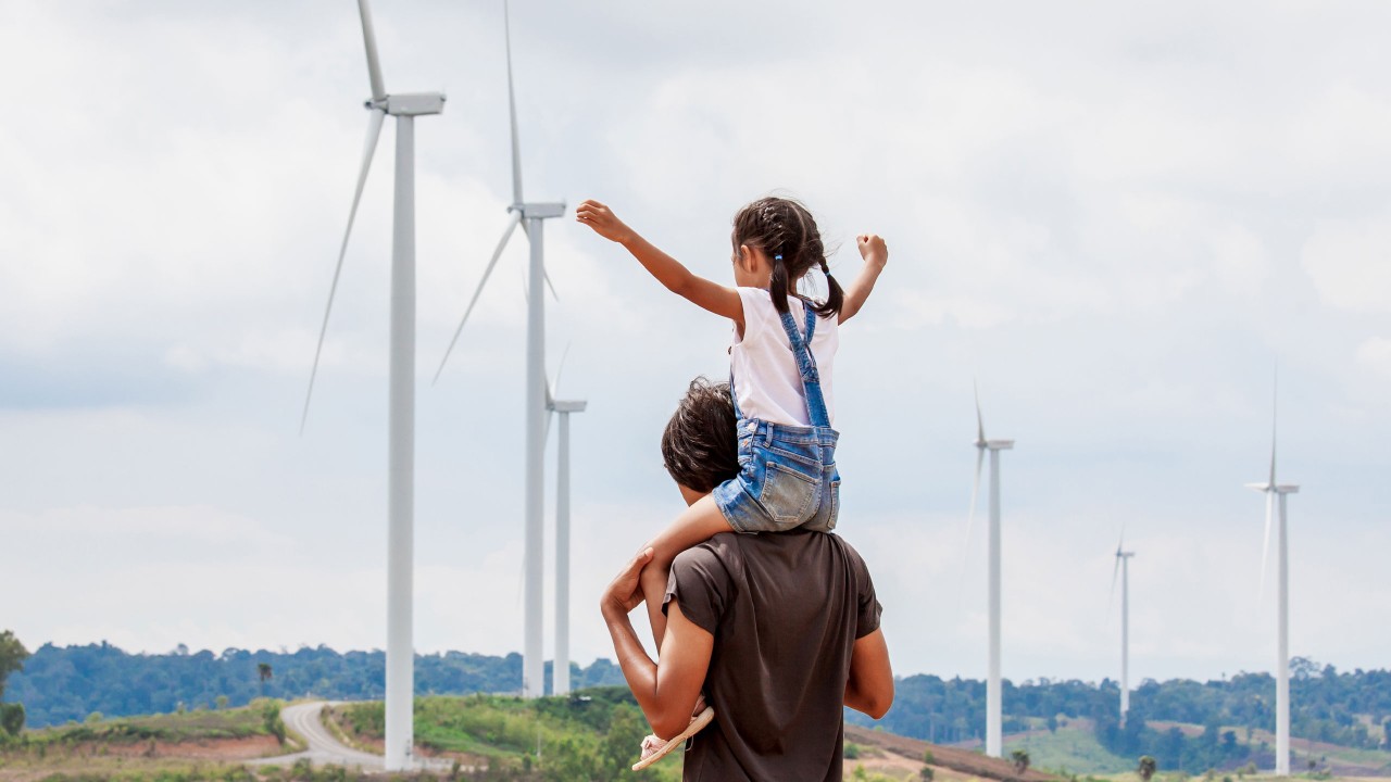 一對父女在騎脖子觀看着風車發電機；圖片使用於滙豐One能投資講堂頁面。 