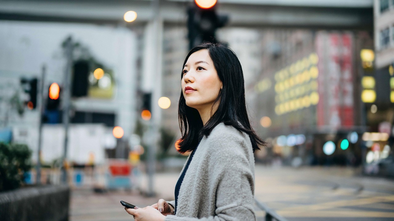 一位女士正拿著手機在街道上尋找方向; 圖片使用於滙豐台灣One能補給站的頁面。