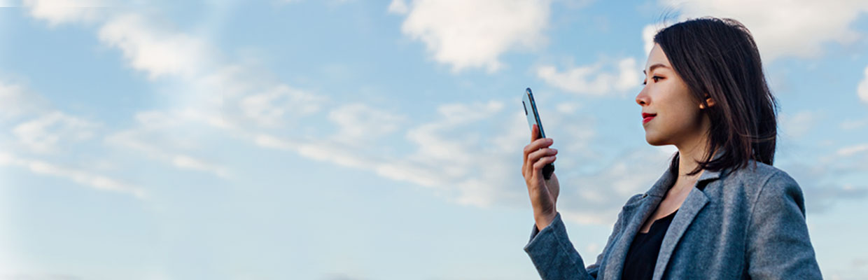 一位女士在藍天下使用手機; 圖片使用於帳單與繳費的頁面。
