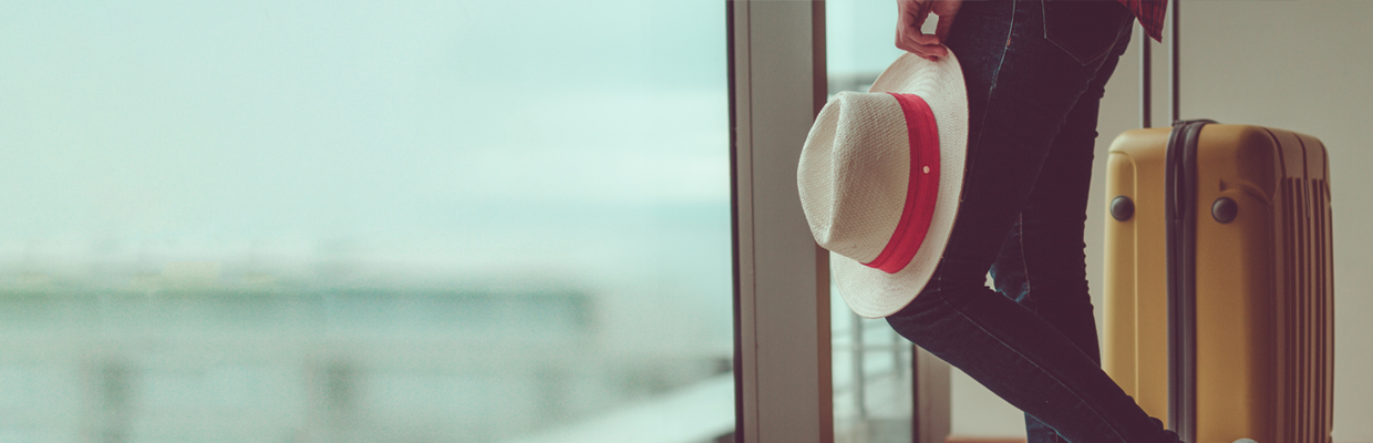 一個人攜著帽子及行李箱站在窗戶旁; 圖片使用於滙豐台灣機場貴賓的頁面。