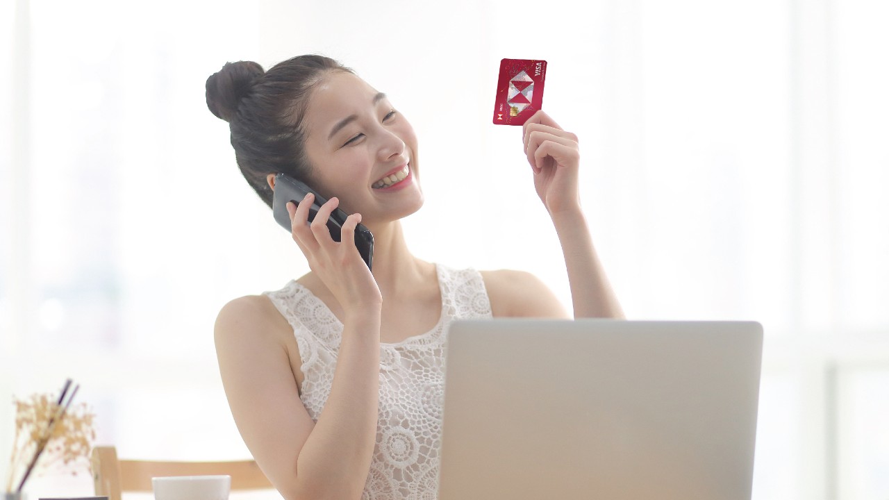 A woman is smiling and calling and looking at a card; image used for HSBC Taiwan HSBC Co-Brand Credit Cards page.