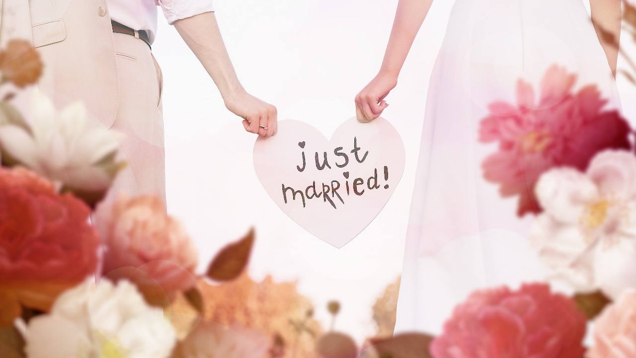 A couple is holding a heart shaped cardboard with Just Married written on it; image used for HSBC loans article - how to plan a dream wedding.